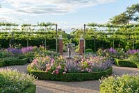 A formal, box edged, sunken rose parterre. Central bed of Rosa 'Louise Odier' and catmint. Outer beds of roses, salvias, astrantias and Geranium 'Blue Cloud'. Pleached crab apple trees contain space.