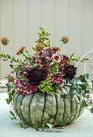Flower filled green pumpkin on table with Dahlias, Zinnias, Ivy, October. 