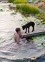 Boy playing in the 'natural' swimming pool with pet dog by wooden jetty
