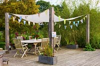 Wooden decking seating area with pergola fitted with shade sail and bunting
