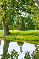 View across water to sculpture in stainless steel set against garden backdrop