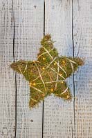 Moss star decorated with small LED lights hanging next to rustic wooden surface