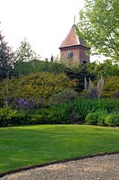 John Brookes garden, 'Denmans' near Chichester, West Sussex, England. Curving lawns, gravel paths, shrub borders and clock tower