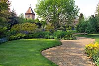 John Brookes garden, 'Denmans' near Chichester, West Sussex, England. Curving lawns, gravel paths, shrub borders and clock tower