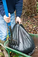 Making compost from collected leaves in a black bin. Using a fork to puncture the bag to allow air to enter