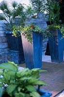 Tall grey zinc planters with planting including Pelargonium Canna Plumbago Hosta palm Courtyard patio of stone paving gravel