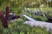 Chelsea Show Garden with water feature, tree fern foliage, perennial planting, wall of steel rings or circles by Andy Sturgeon