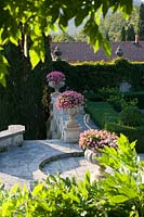 Villa La Foce, Tuscany, Italy. Large garden with topiary clipped Box hedging and views across the Tuscan countryside, pink pelargoniums in classical urns