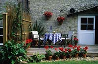 private garden Sussex Design Alan Titchmarsh small deck with table and chairs red pelargoniums in pots