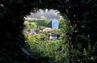Tilford Cottage Surrey View of formal herb garden through circular window in yew hedge