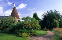 The Oast Houses Hampshire curved gravel path and lawns with mixed shrub borders view of house