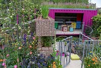 The Montessori Centenary Children's Garden  a view through the gate leading to childrens classroom and play area. Plants include:  Red Campion - Silene dioica growing on the roof,   Designer: Jody Lidgard, Sponsors: Montessori Centre International. RHS Chelsea Flower Show 2019