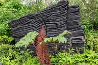 The M and G Garden. Blackened timber sculptures by Johnny Woodford, creating a dramatic backdrop for green woodland planting. Awarded an RHS Gold Medal. Designer: Andy Sturgeon. Sponsor: M and G - Chelsea Flower Show 2019