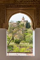 View of gardens and church through ornate stone-carved archway, Generalife Gardens. The Alhambra, Granada.