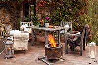 Garden table, chairs and fire basket on terrace set up for evening entertaining, Le Mas de BÃ©ty, France. 
