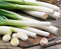 Allium porrum, Leeks, on wooden surface with chopping board and knife.