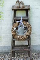 Ladder with wreath, watering can and clogs.