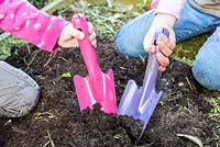 Children digging with colourful gardening trowels. 