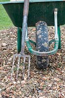 Gardening fork and wheelbarrow on a wood chip path. 