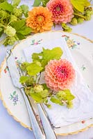 Table setting with orange and peach dahlias and Humulus lupulus