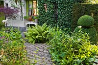 Paved courtyard with perennials, grasses and box topiary. Dina Deferme garden, Belgium
