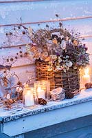 Dried seedheads, including hydrangeas, honesty, nigella, wheat and poppies, in a willow basket with tealights