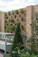 Bench next to pots hanging from a wire grid, attached to a brick wall