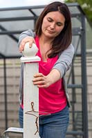 Woman attaching a wooden finial to a wooden post. 