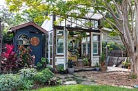 View of conservatory and charcoal grey painted outhouse in Australian garden. 