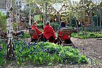 Three ladies with red blankets around their shoulders sitting in the Dalston Eastern Curve Garden, London Borough of Hackeny, UK. 