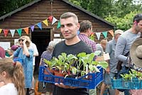 Man holding crate of vegetables at Alexandra Palace Allotments plant sale, London, UK. 