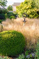 Circular bed with clipped box sphere and a sundial with Deschampsia caespitosa 'Goldschlier', Gold Veil, Newport, Wales.