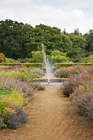 Fountain on gravel paths with mixed perennials, Scampston Hall, North Yorkshire, UK