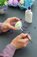 Woman using a brush and glue to fix Primrose petals on to eggshell as decoration