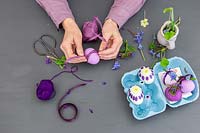 Woman adding purple raffia to purple coloured eggshell as decoration