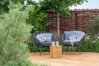 Willow woven fence with chairs on oak decking, Salix rosmarinifolia in foreground and Corylus avellana and Acer campestre behind - Raised by Rivers, RHS Tatton Park Flower Show 2018