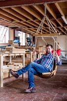Chris Punch, garden furniture designer in workshop, with swing chair.