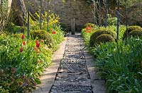 Pebble mosaic path with red tulips 'Apeldoorn' in adjoining beds at Barnsley House, Cirencester, UK