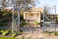 View through metal gate to The Temple, used as a summerhouse, beside the pond at Barnsley House, Cirencester, Glos, UK. 