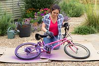 Woman spraying old childs bike with purple paint