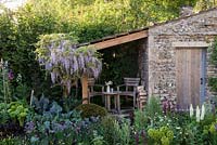 Wisteria sinensis, table and chairs, Lupinus 'Masterpiece', Euphorbia, clipped Taxus baccata, Chives, Kale Cavolo Nero and Leeks -  Welcome to Yorkshire Garden - Sponsor: Welcome to Yorkshire - RHS Chelsea Flower Show 2018