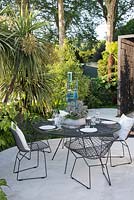 Cordyline australis with metal table and chairs. VTB Capital Garden - Spirit of Cornwall, RHS Chelsea Flower Show, 2018. Sponsor: VTB Capital