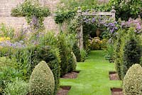 View of grass path framed by formal topiary and flowerbeds. 