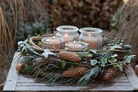 An Advent wreath on a table in the garden bonded out of Pinus strobus cones, 
pine green, ivy Hedera helix, clematis cirrus, covered by powder snow or white 
frost. Inside the wreath you find 4 candles in lanterns.