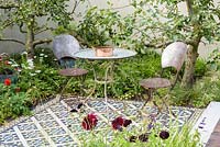 Table and chairs on mosaic tiled patio. 'Style and Design Garden', RHS Hampton Flower Show 2018