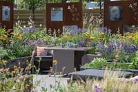 Outdoor Rattan dining furniture surrounded by colourful planting  - RNIB's Community Garden, RHS Hampton Court Palace Flower Show 2018