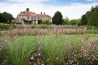 View across flowerbeds of Miscanthus sinensis 'Kleine Silberspinne' and Gaura lindheimeri 'Rosyjane' to house. Heale House, Middle Woodford, Salisbury, Wilts, UK.
