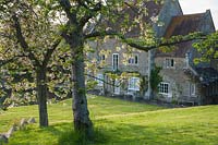 View of converted mill, through branches of blossoming trees. Job's Mill, Crockerton, Wiltshire, UK. 