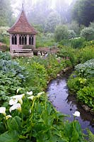 Summerhouse in the bog garden by a stream fringed with moisture loving plants. The Old Rectory, Netherbury, UK.