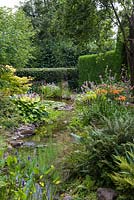 View of a pumped stream, edged in astilbes, daylilies, hostas, ferns and primulas.